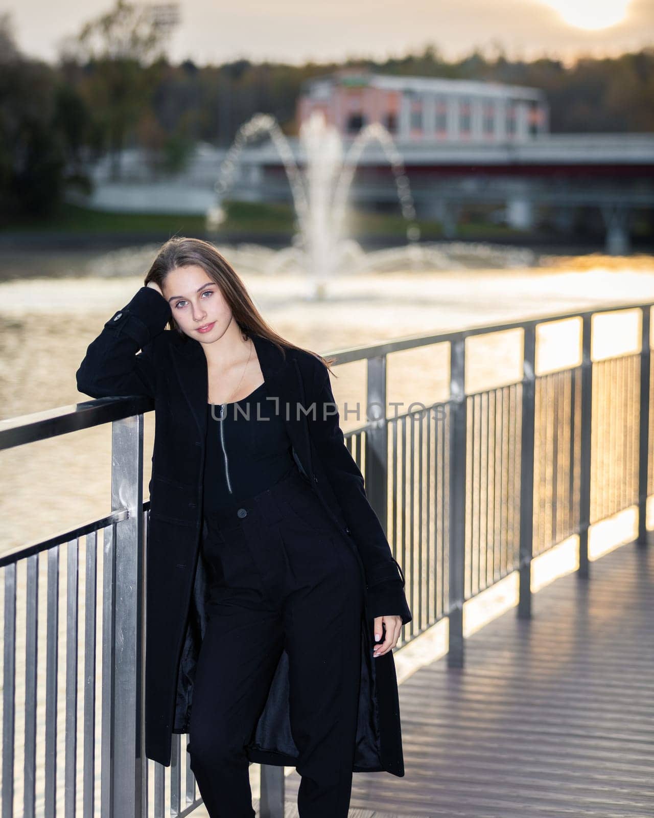 Portrait of a girl on a bridge near a pond in a city park against the backdrop of fountains