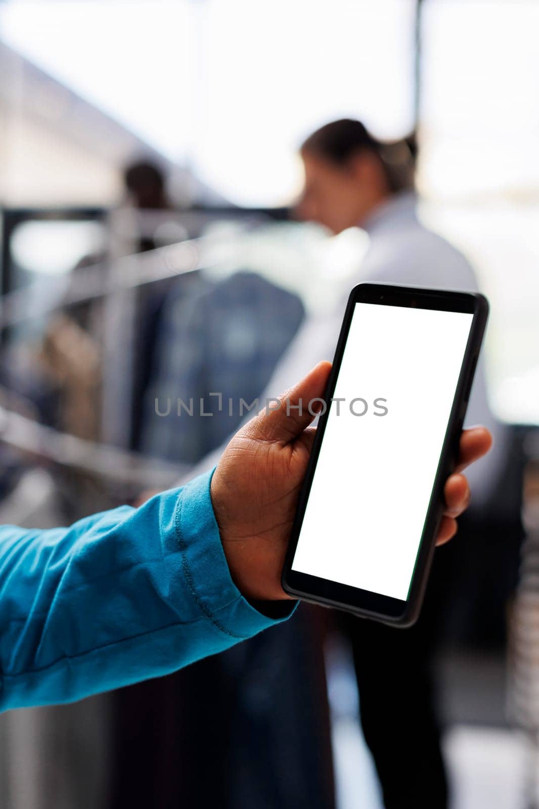 Selective focus of mobile phone with white screen, african american customer holding digital device in modern boutique. Stylish woman shopping for fashionable merchandise in clothing store