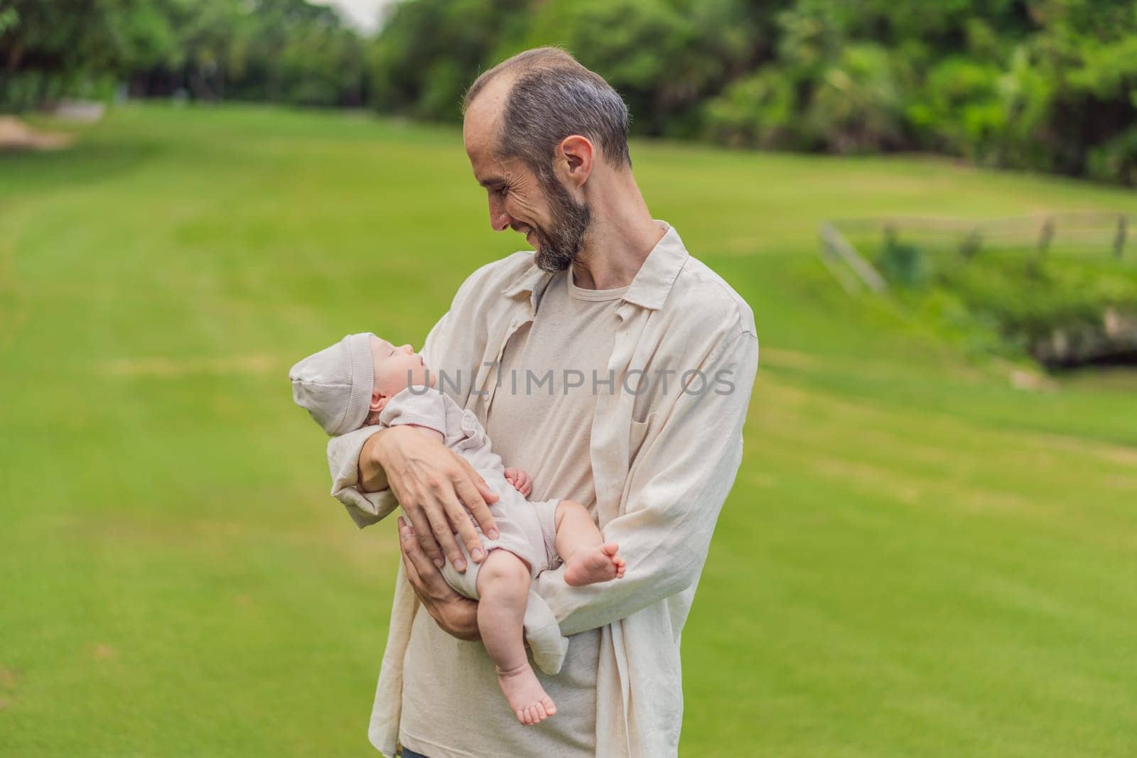 A happy 40-year-old father cradles her newborn in a sun-drenched park. Love, family and generations in harmony by galitskaya