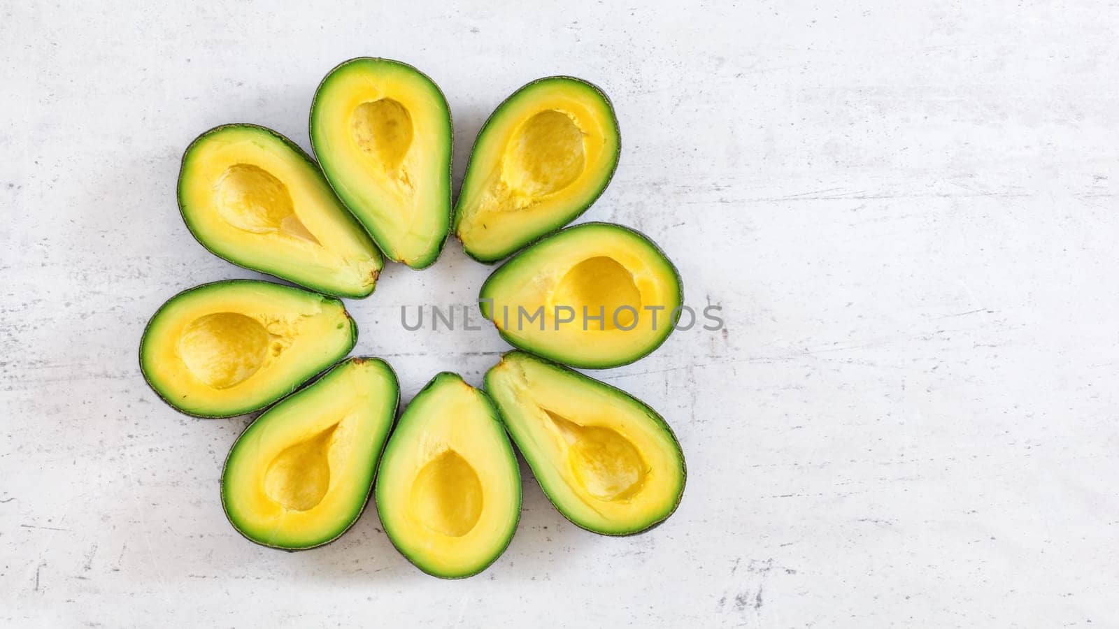 Top down view, 8 avocado halves arranged in circle on white board, banner with space for text right