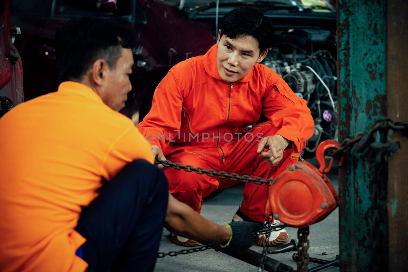 Mechanic testing strength and reliability of chain hoist for car towing in car workshop garage. Automotive service worker ensure through inspection of mechanical equipment. Oxus