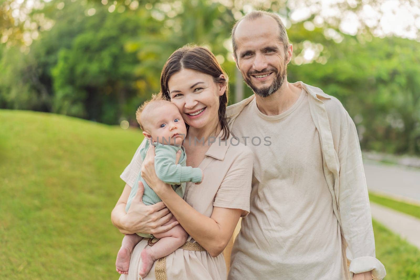 A happy 40-year-old couple cradles their newborn in a sun-drenched park. Love, family and generations in harmony.