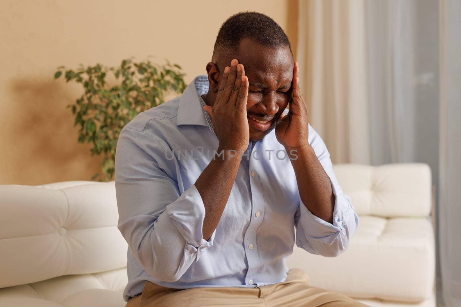 african american guy holding his head and suffering from headache and migraine at home, stress at home