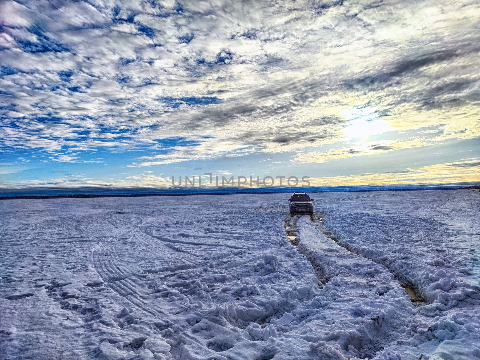 The snowy road stretches alongside a river with melting ice, highlighting winter activities in Arkhangelsk and the expansive sky above.