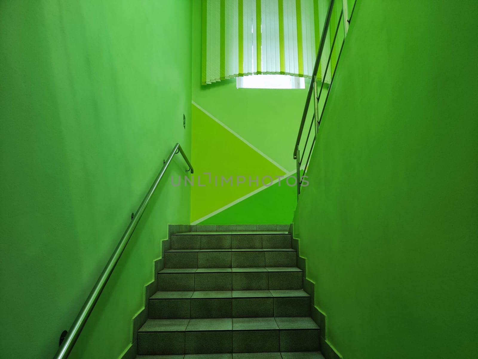 A well-lit green staircase leads down to door in a contemporary structure