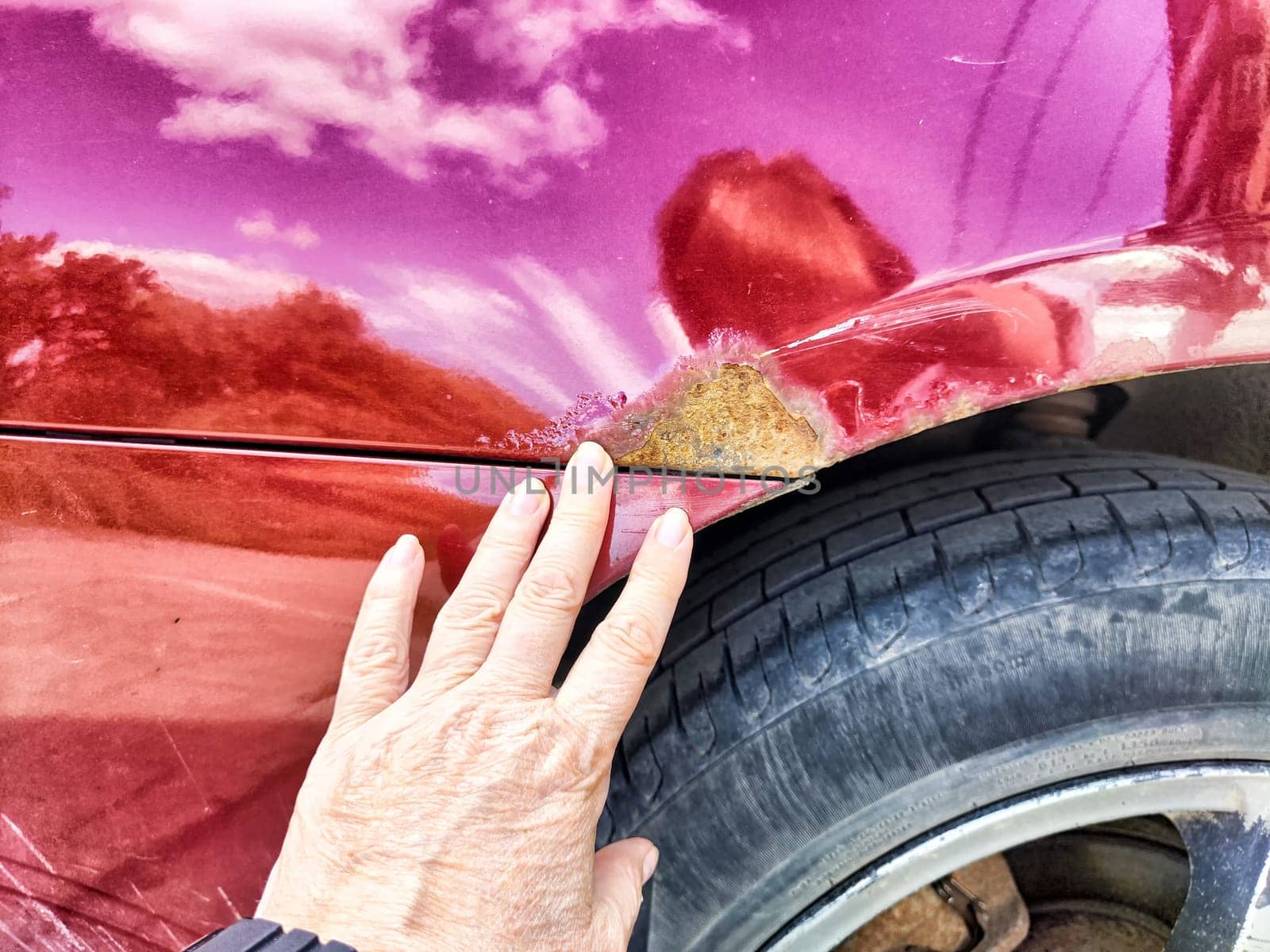 A person is pointing directly at a rusty, weathered place on a car that shows signs of age and decay, highlighting its condition