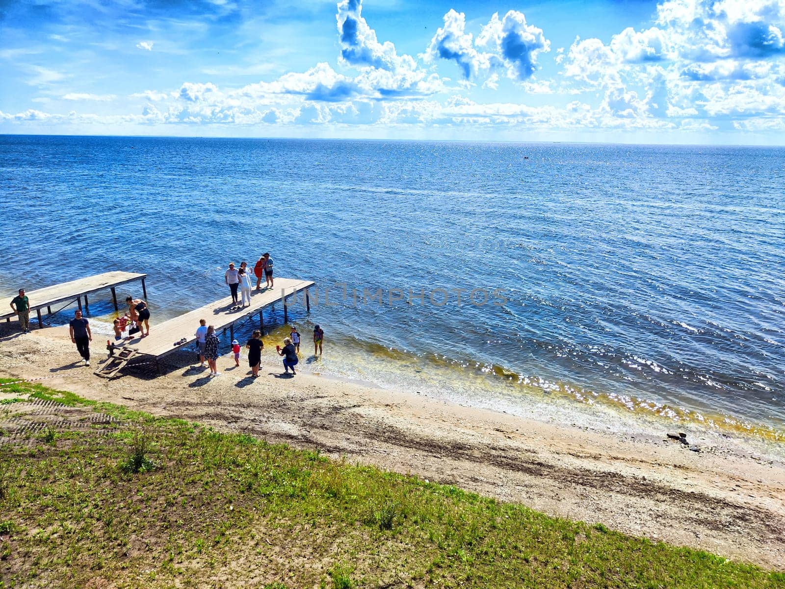 Groups of individuals gather on docks by the water's edge, soaking in the sun and enjoying the clear blue skies on a warm day.