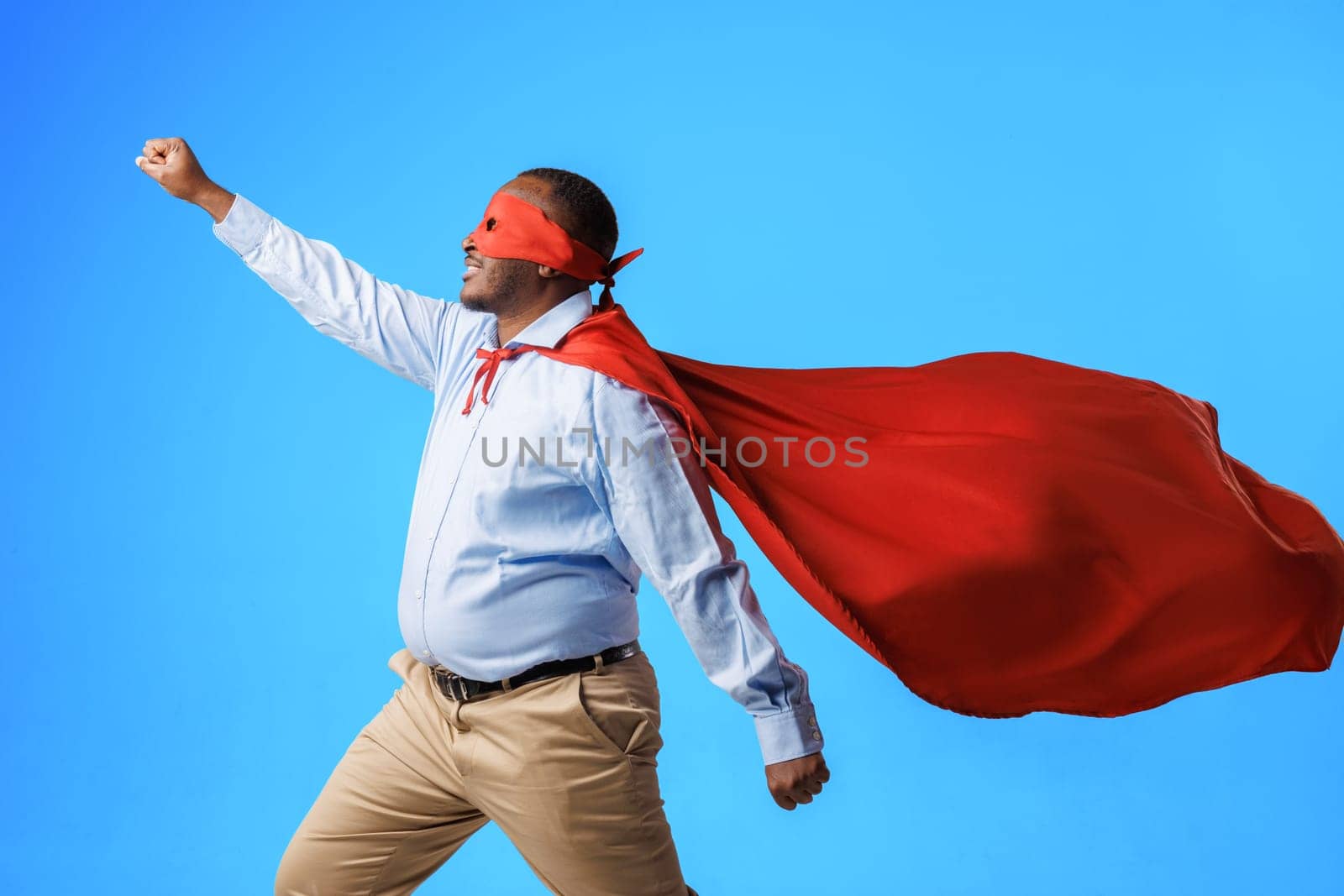 African American overweight guy in superman costume, in flying pose on blue background, concept of speed, superpowers and super abilities