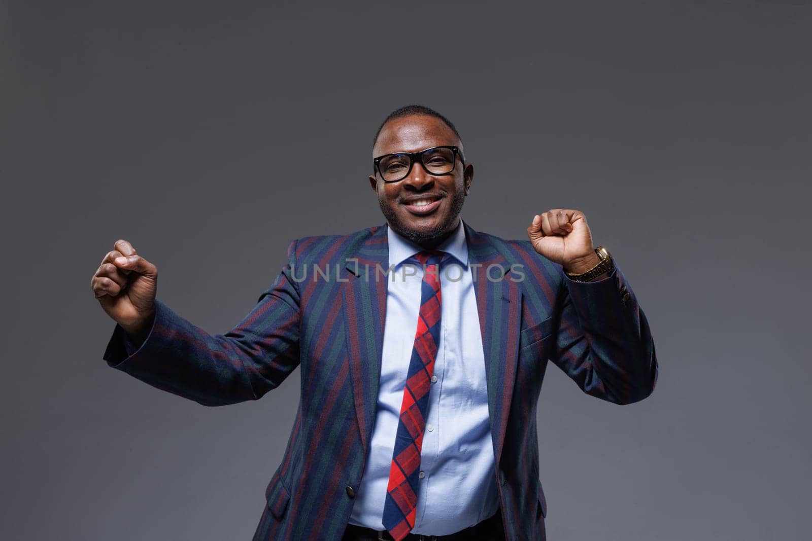 Handsome cheerful African businessman dancing from a hasty deal, on gray background, concept of successful business