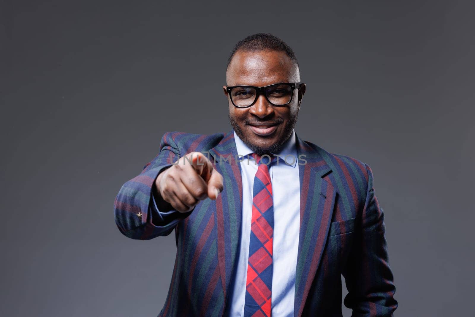 confident african businessman in suit and tie pointing finger at viewer on clear grey background, successful business