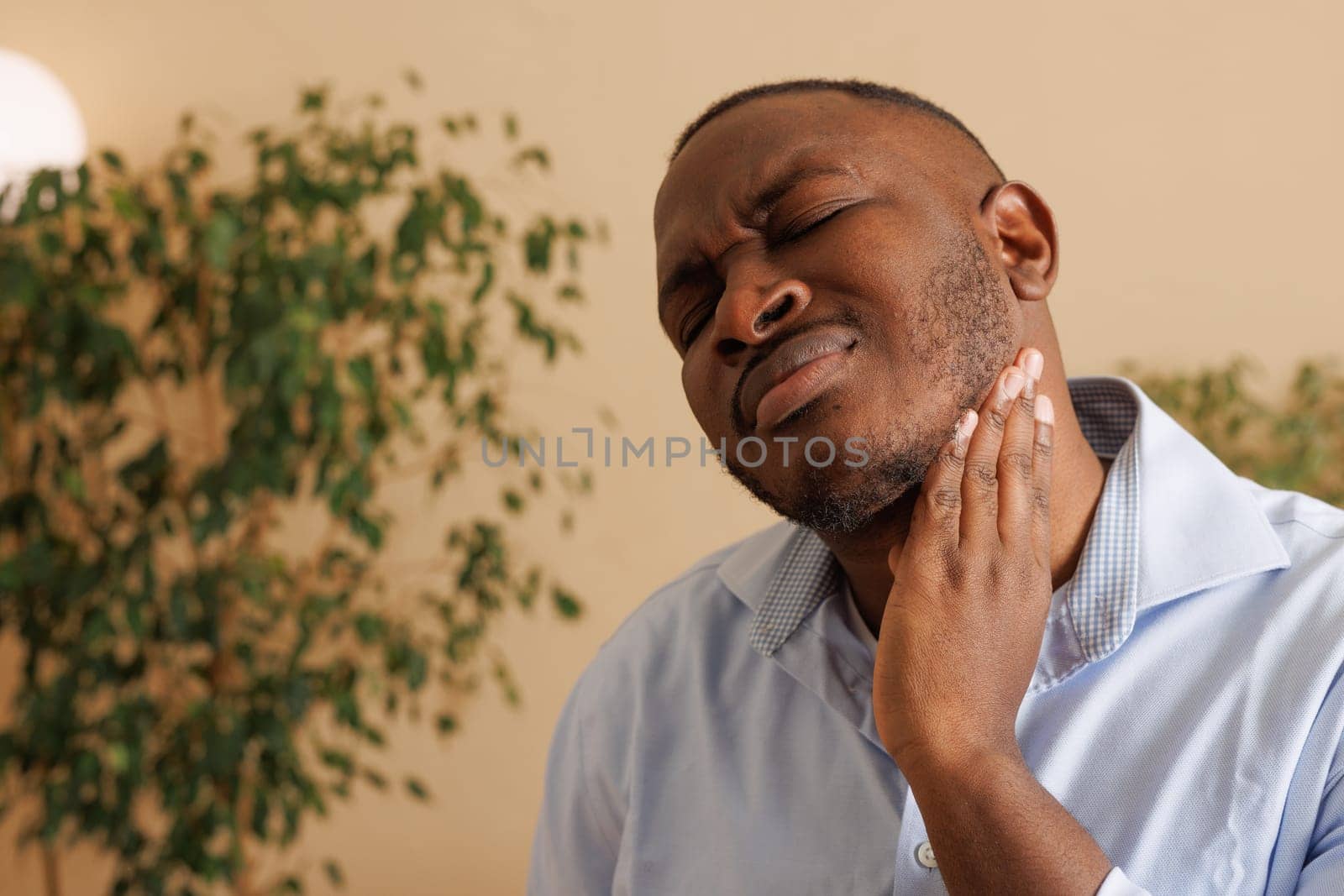 Man sitting on sofa in living room and feeling pain in neck and throat. Cozy home environment. Concept of discomfort, pain relief, home interior.