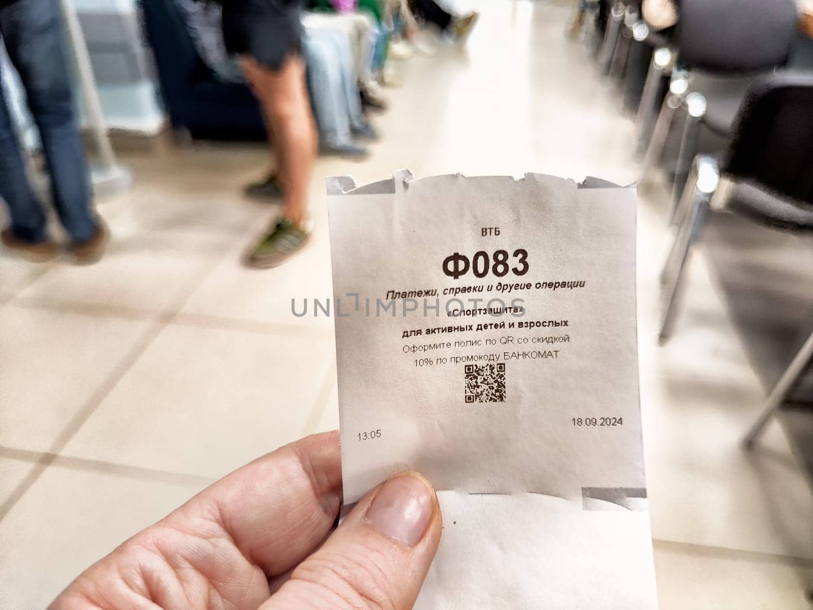 Kirov, Russia - September 18, 2024: A customer holds a ticket indicating their place in the bank's private service queue, navigating through midday busyness.