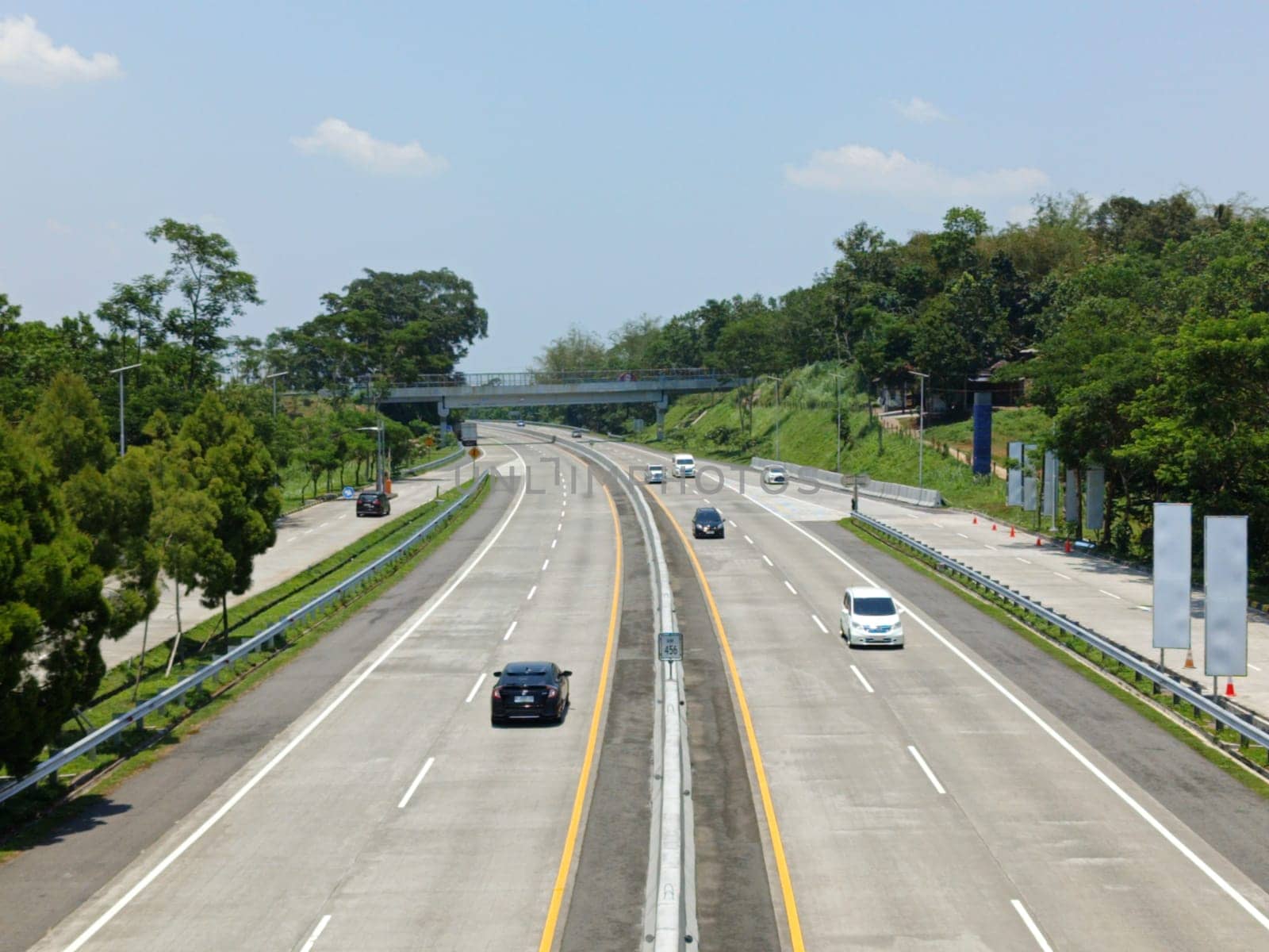 A highway with a bridge over it and cars driving on it. The cars are mostly white and black