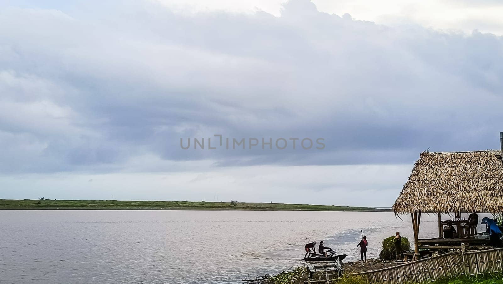 A beach with a small hut and a boat in the water. The sky is cloudy and the water is calm