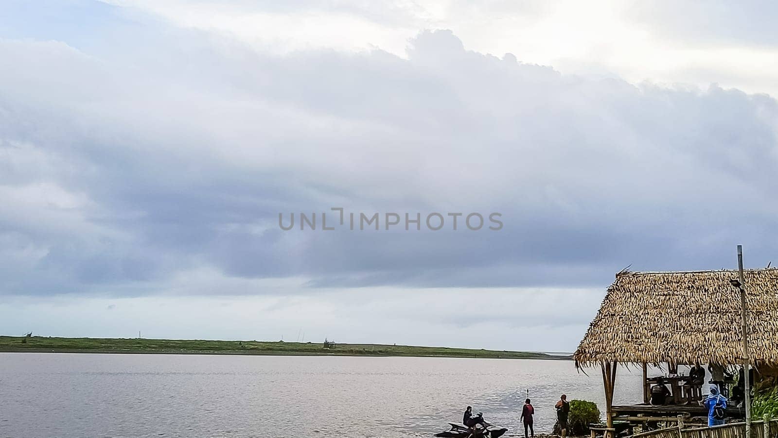 A beach with a small hut and a boat in the water. The sky is cloudy and the water is calm