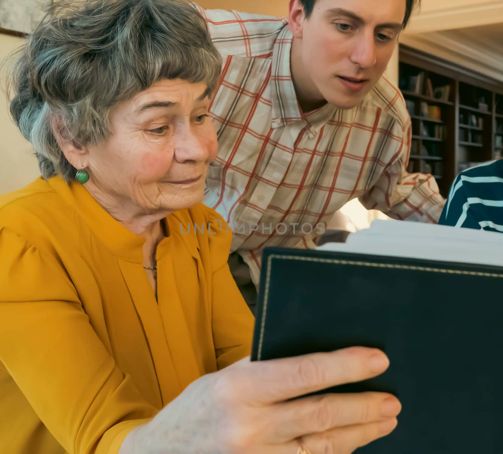 Family smiles happily and spends time together at home, young girl and a man look at photo album with their grandmother, help an elderly woman remember her youth, visit and take care of grandparents.