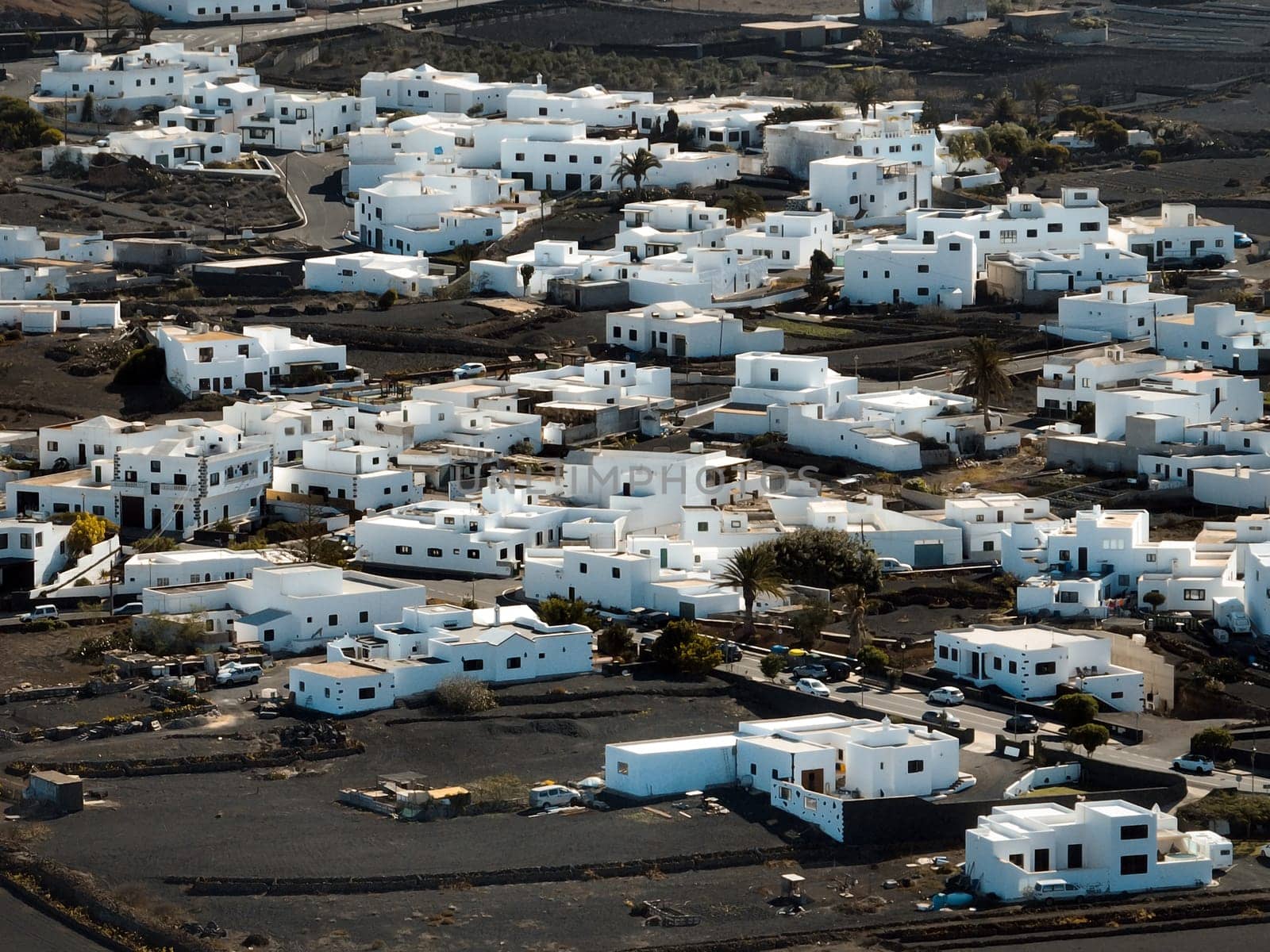 Stylish white buildings and roofs, small towns in Lanzarote among volcanic mountains, black hills and lava formations, aerial photo from above, drone view of villages, travel to the Canary Islands.