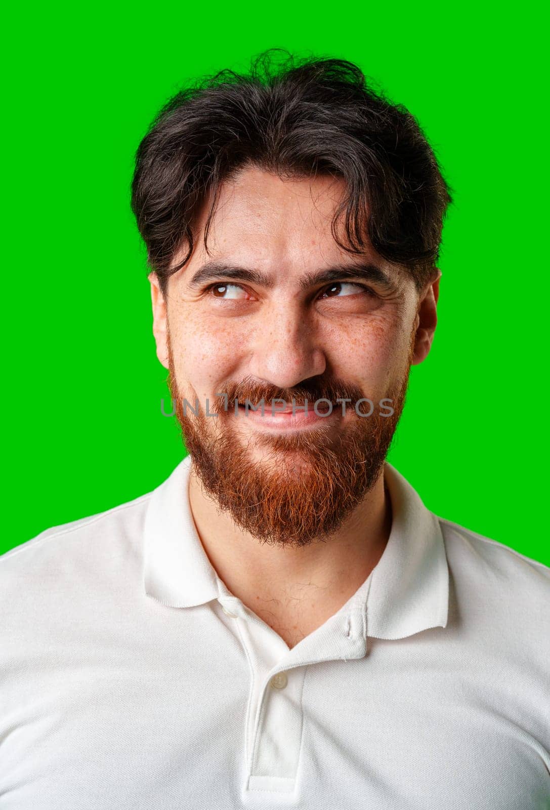 A young man with a beard showing a serious expression against a vibrant green background close up