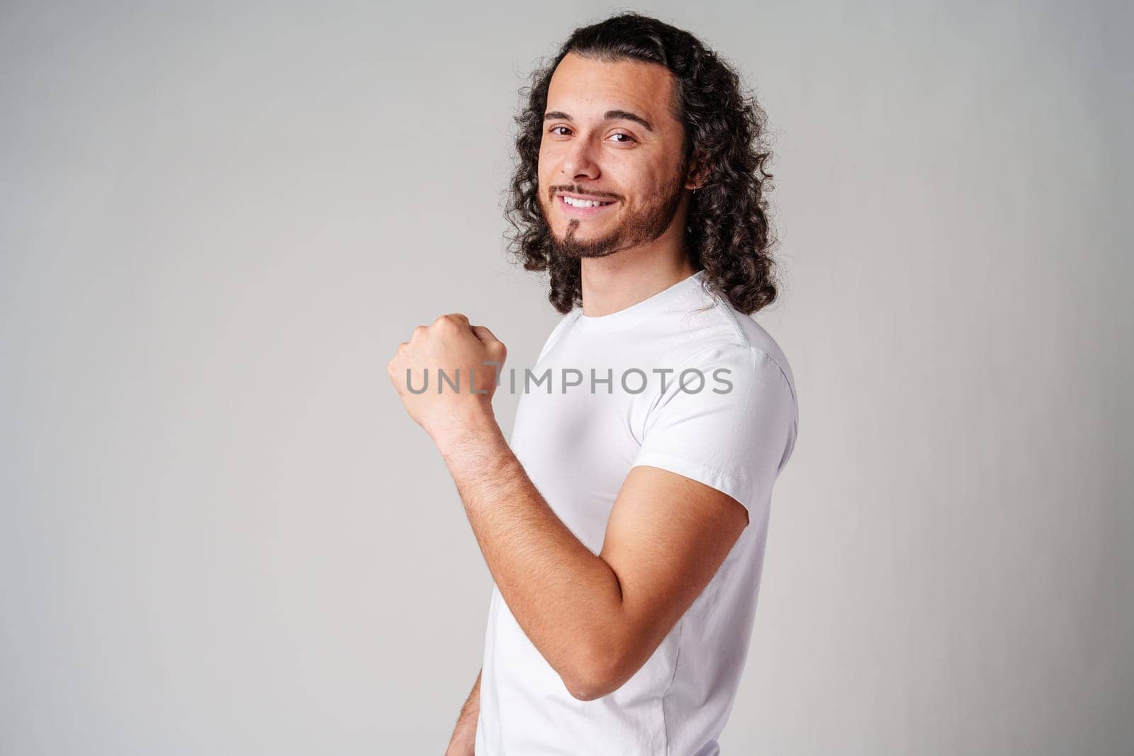 Happy man celebrating success with raised fists in a studio against a plain background close up