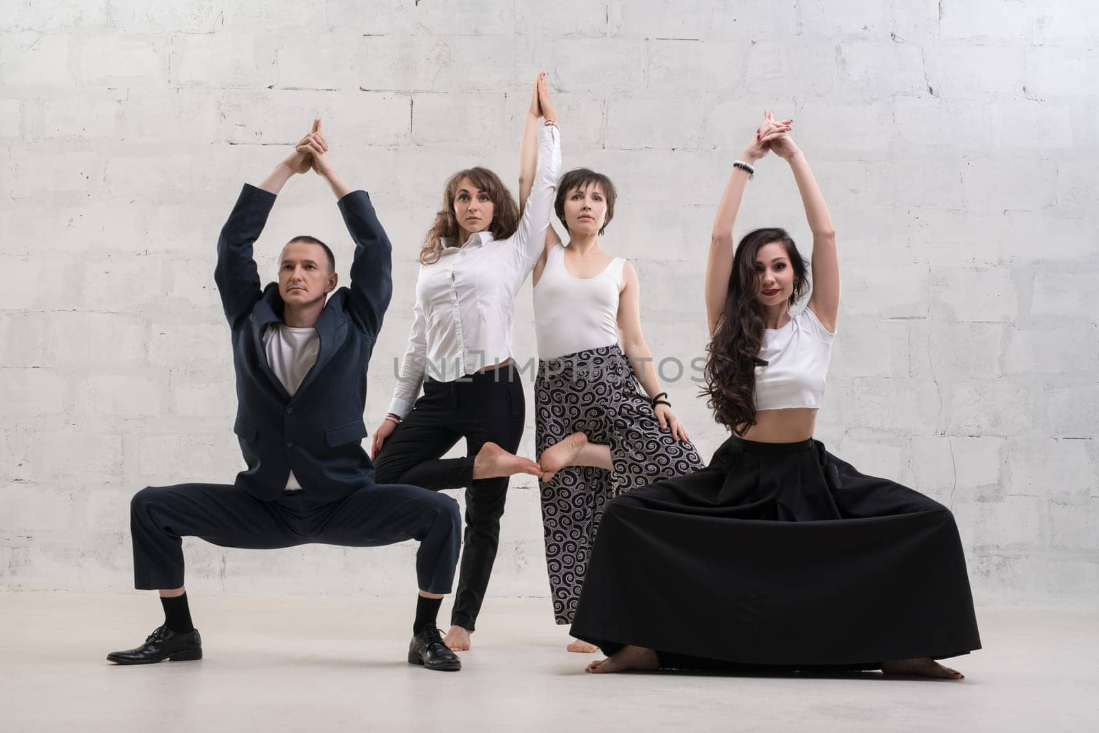 People wearing office clothes doing yoga shot against white brick wall