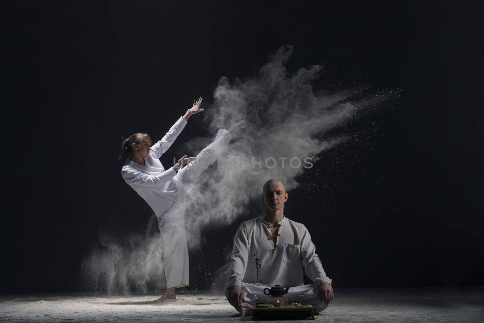 Two male doing yoga in a white dust cloud in dark room full-length view