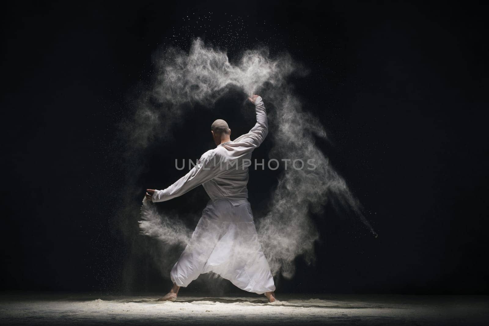 Male doing yoga in white dust cloud in dark room rearview