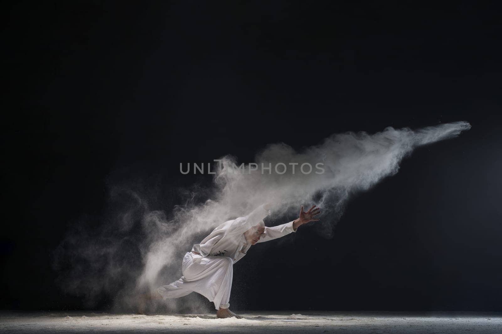 Male doing yoga in white dust cloud in dark room full-length shot - concept of power
