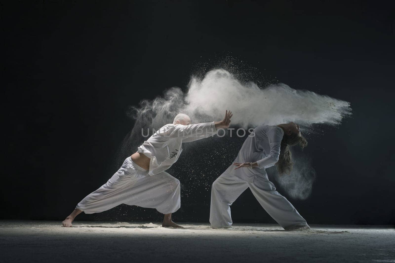 Two male doing yoga in white dust cloud in dark room full-length view