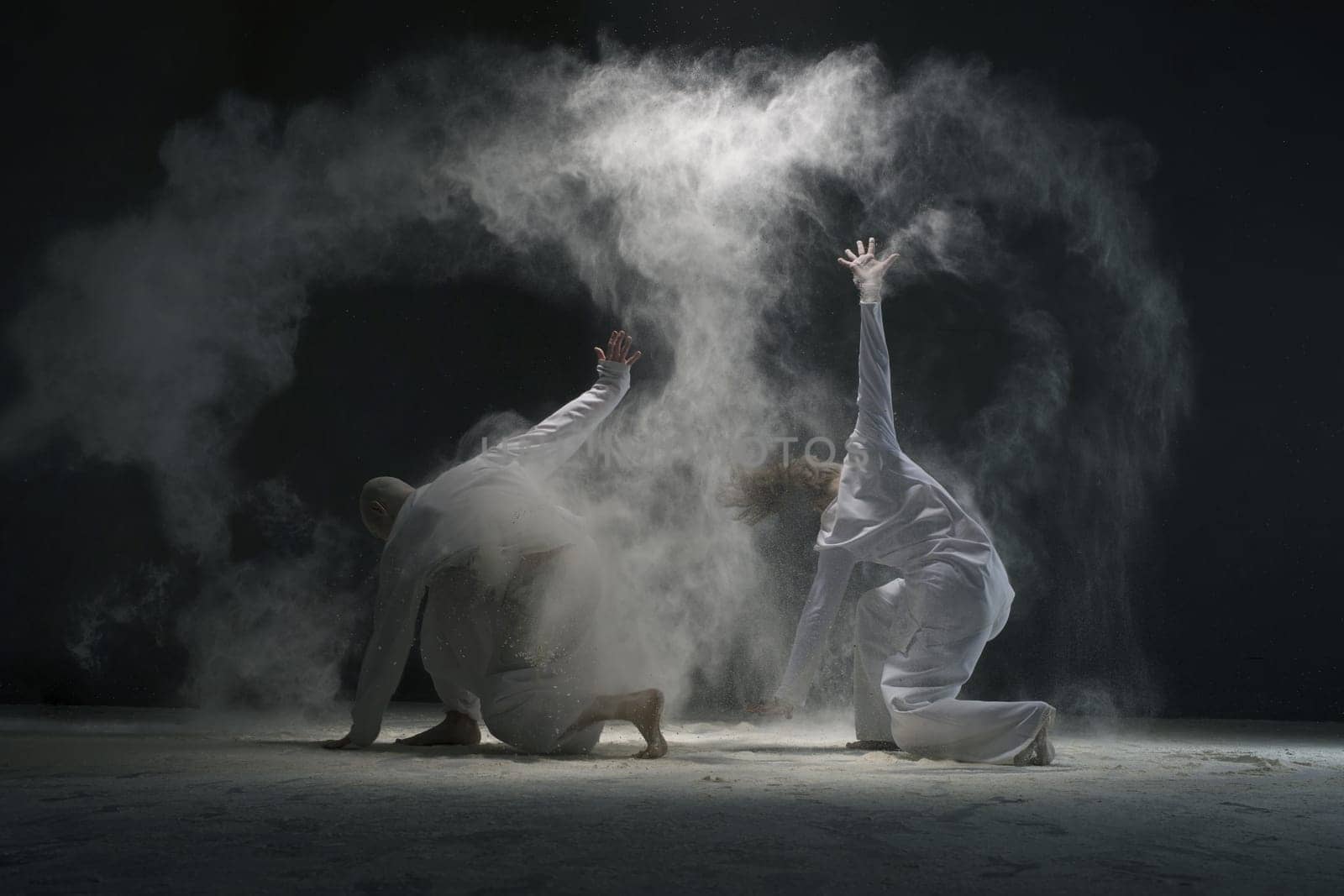 Two men doing yoga in white dust cloud in dark room full-length shot