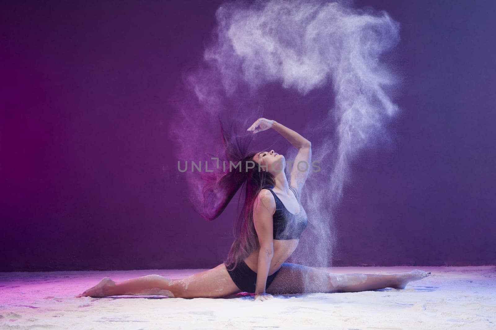Woman sitting in a split in a white dust cloud profile shot