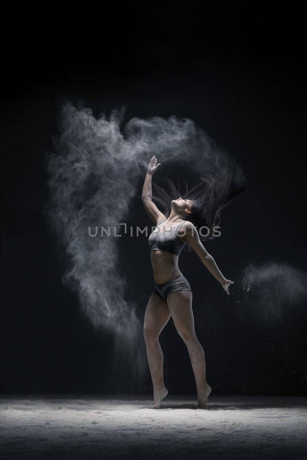 Woman in black shorts and top jumping gracefully in a white dust cloud shot in dark room