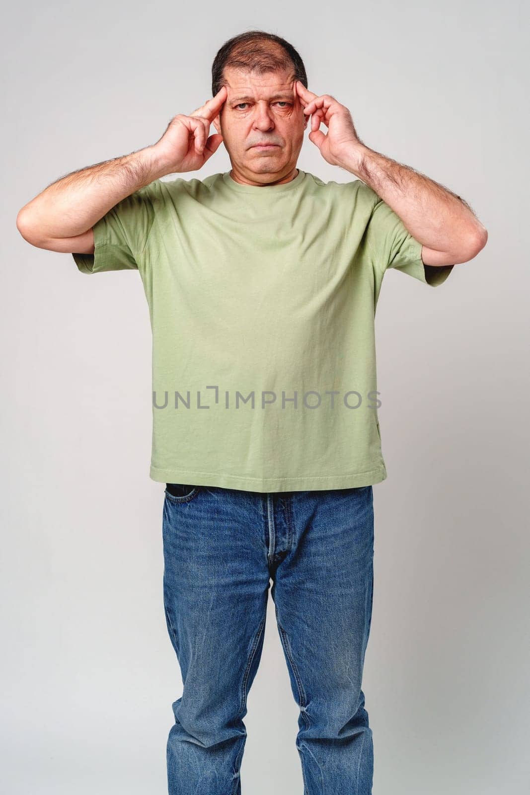 A middle-aged man experiencing stress while holding his head in hands against a neutral background close up