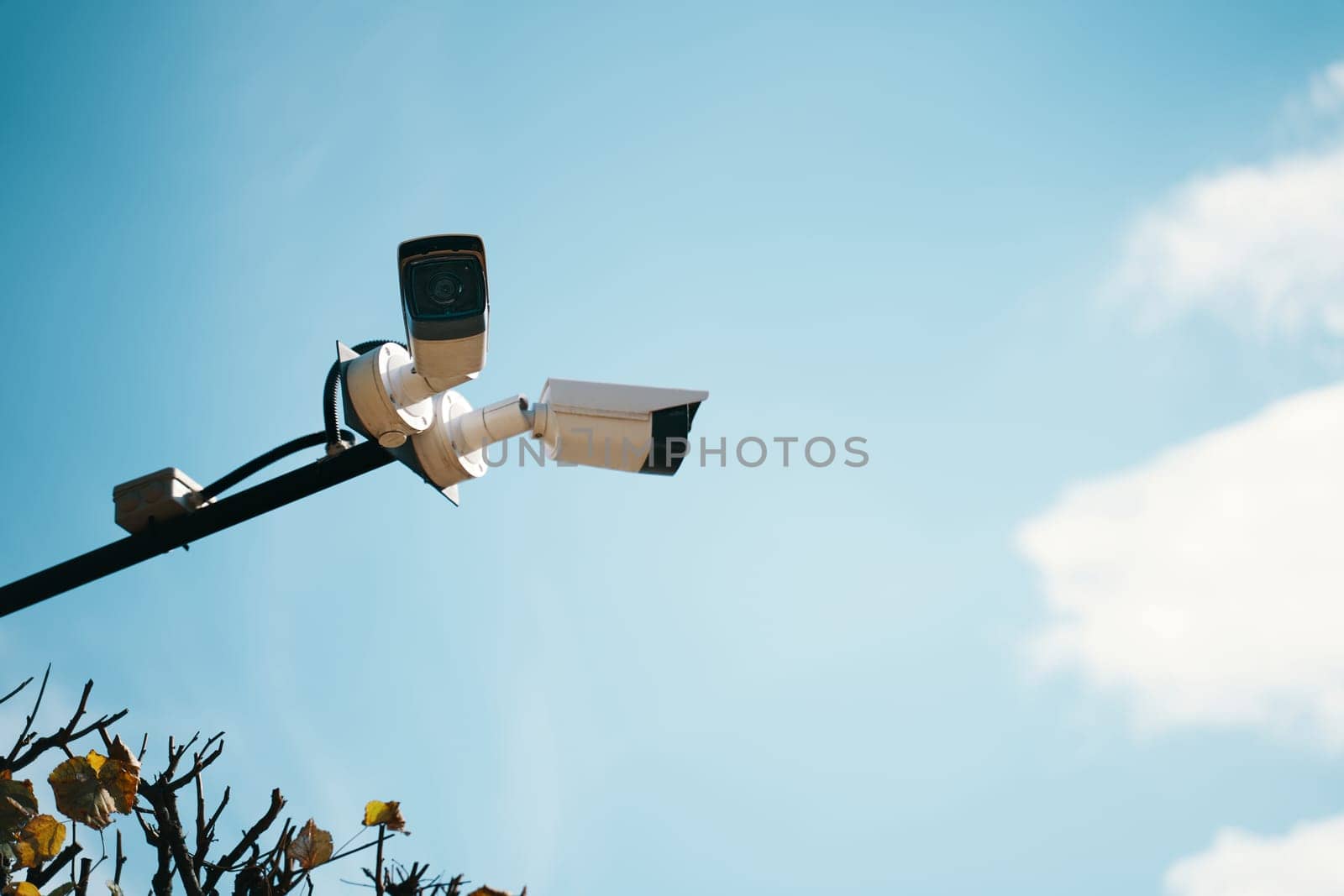 Two surveillance cameras are mounted high on a pole, meticulously observing their surroundings under a bright blue sky