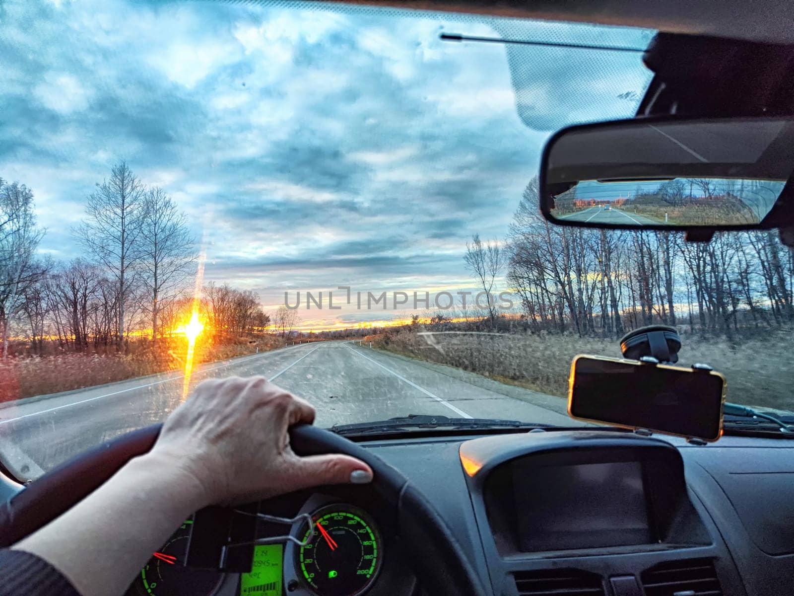Car salon, windshield, hand on steering wheel and landscape in sunset. View from driver on nature with Road. Single traveler. Partial focus. Blurred