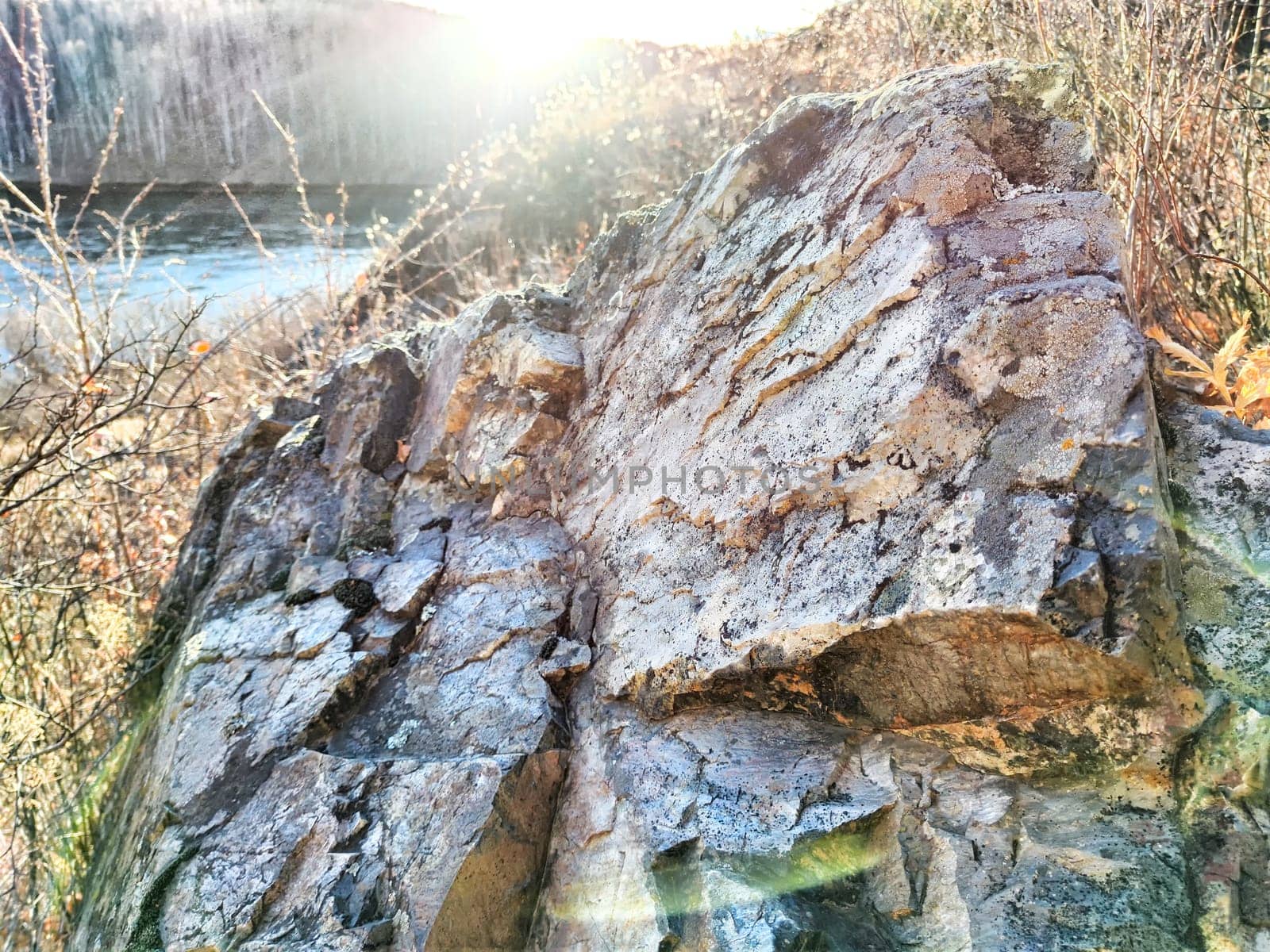 Morning light casts shadows on a textured rock near a winding river.