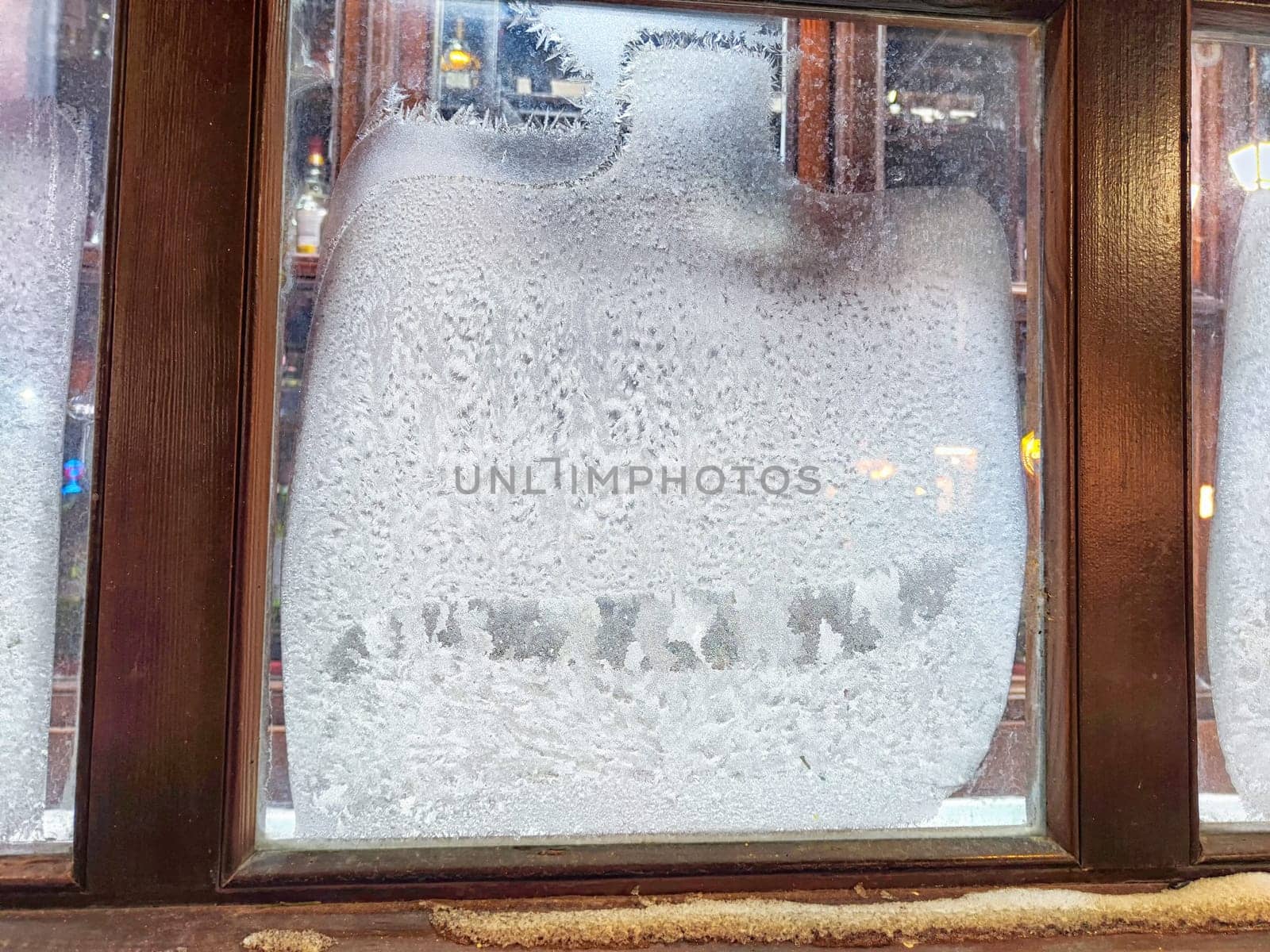 Frost collects on window glass, creating a delicate frost pattern as light shines from inside