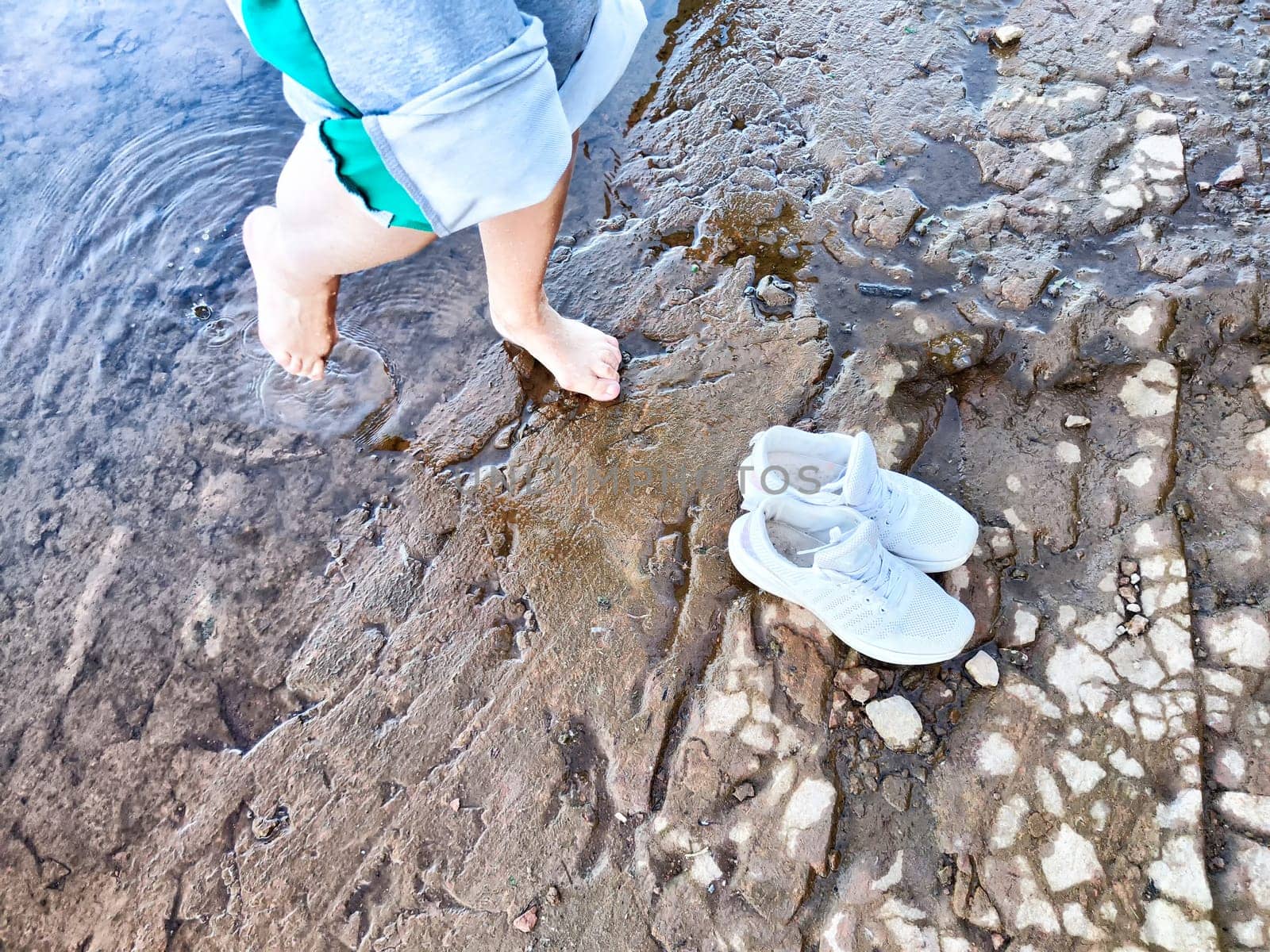 Footsteps in shallow water and shoes resting on dry ground as someone enjoys refreshing moment by the river on a sunny day