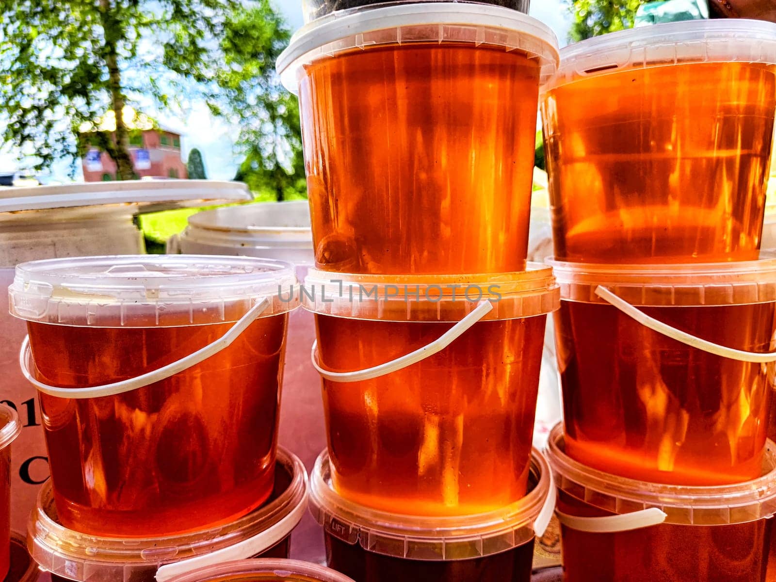 Colorful jelly or honey cups are neatly arranged in a stack at bustling outdoor market on a sunny day