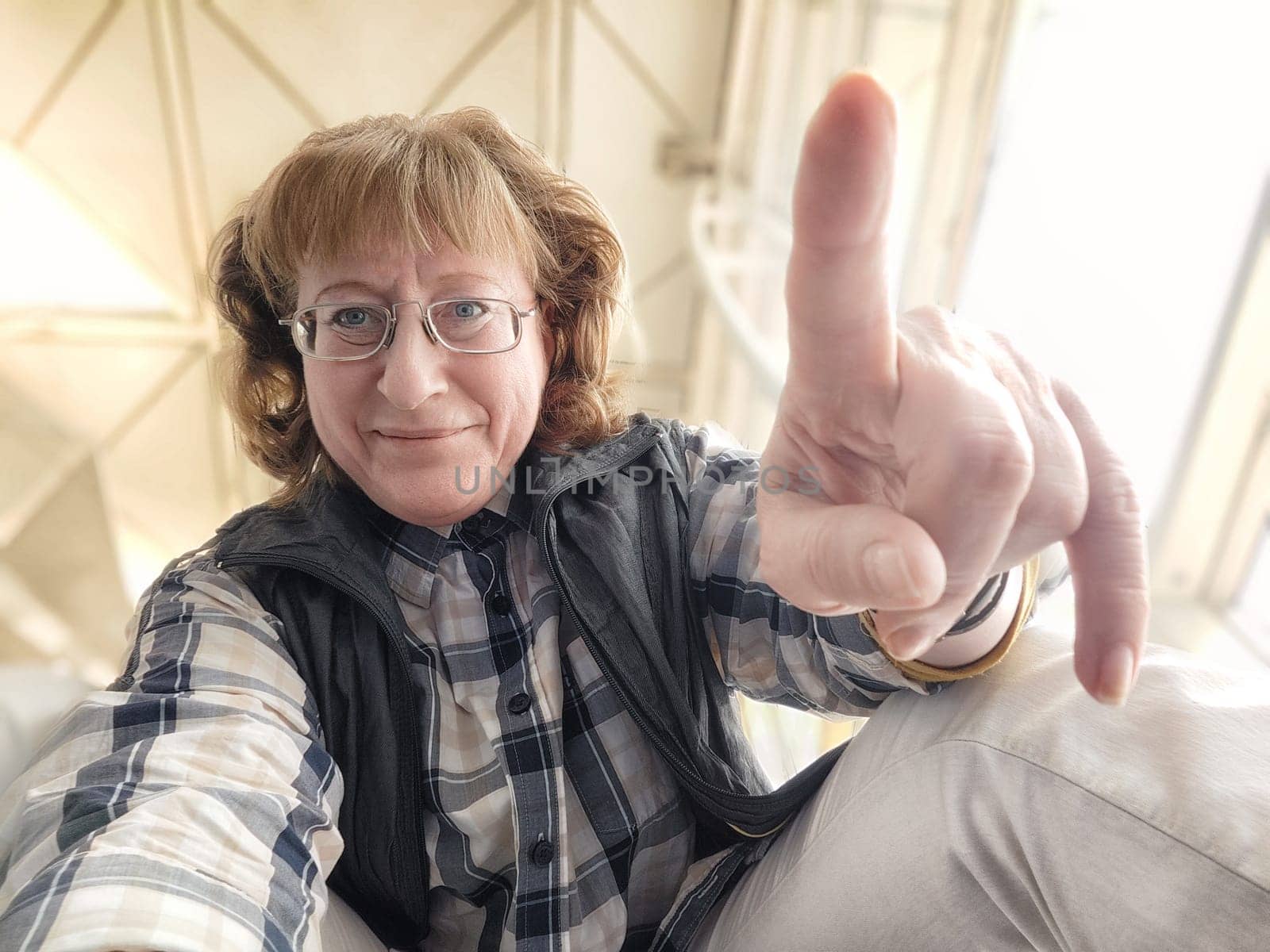 While waiting at the airport, a middle-aged woman enjoys herself by taking a playful selfie, capturing her excitement and the lively atmosphere around her.