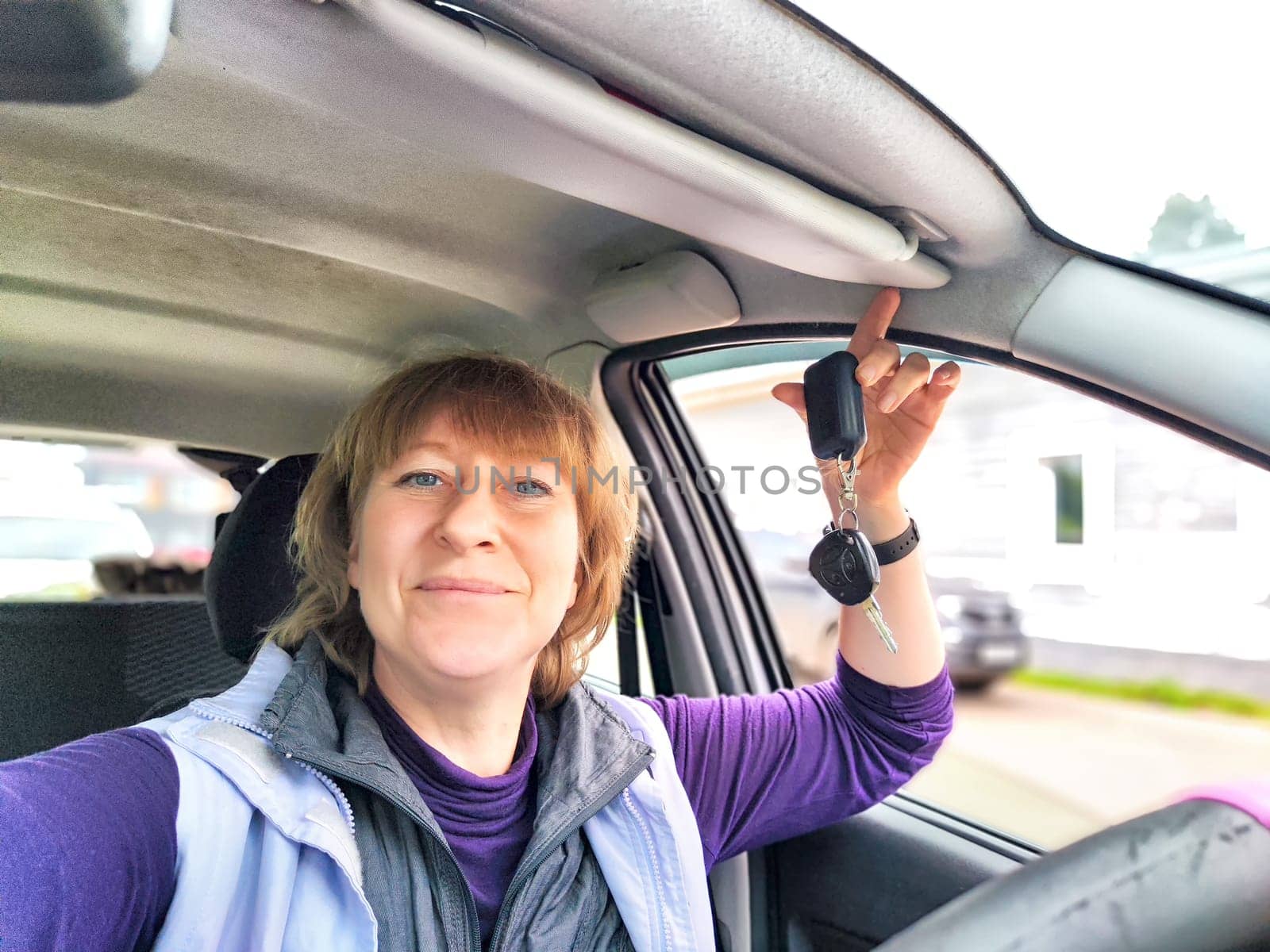 Middle aged woman in a car taking a selfie while enjoying a drive. Female mature driver posing inside car. Funny happy tourist girl in alone travel