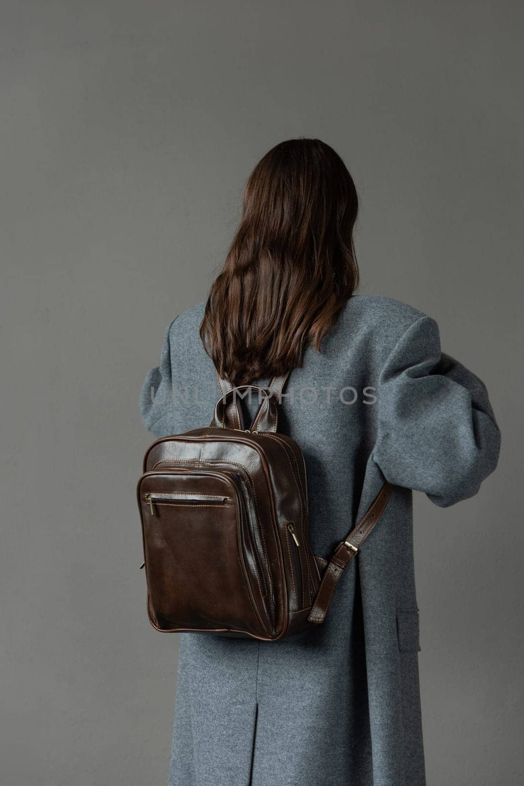 woman posing with a leather backpack wearing a warm gray coat .