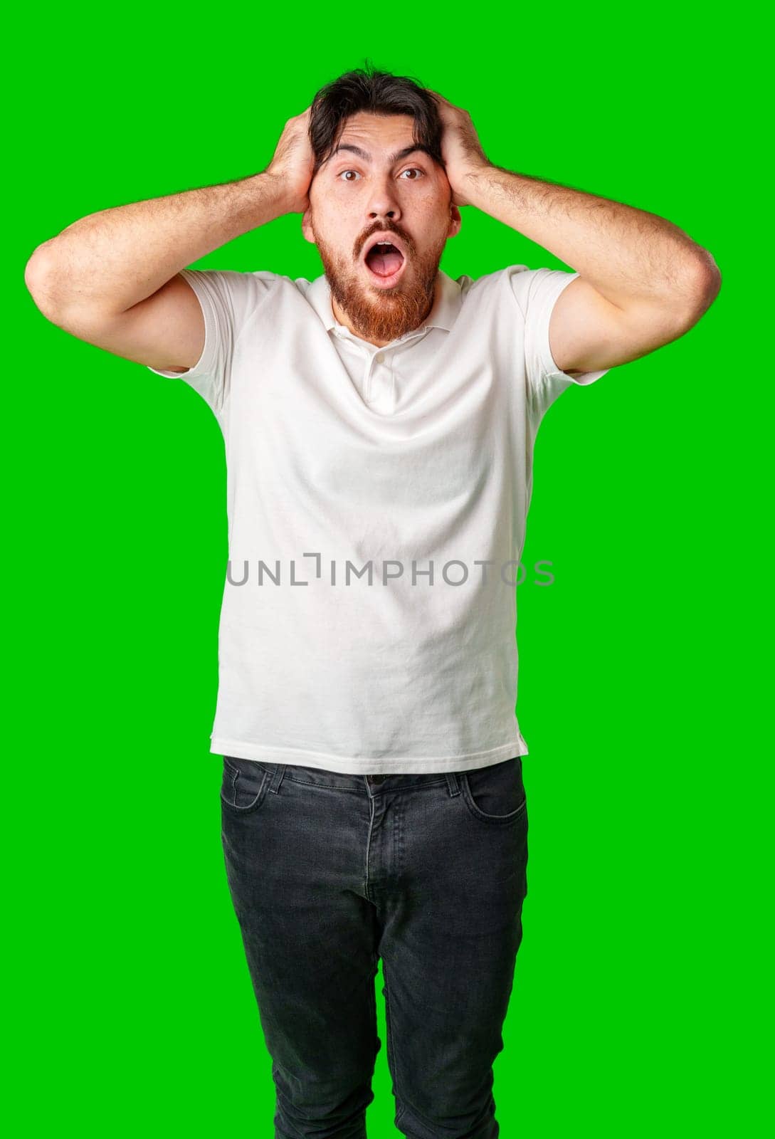 A man with a surprised expression holds his face while against a vibrant green background close up