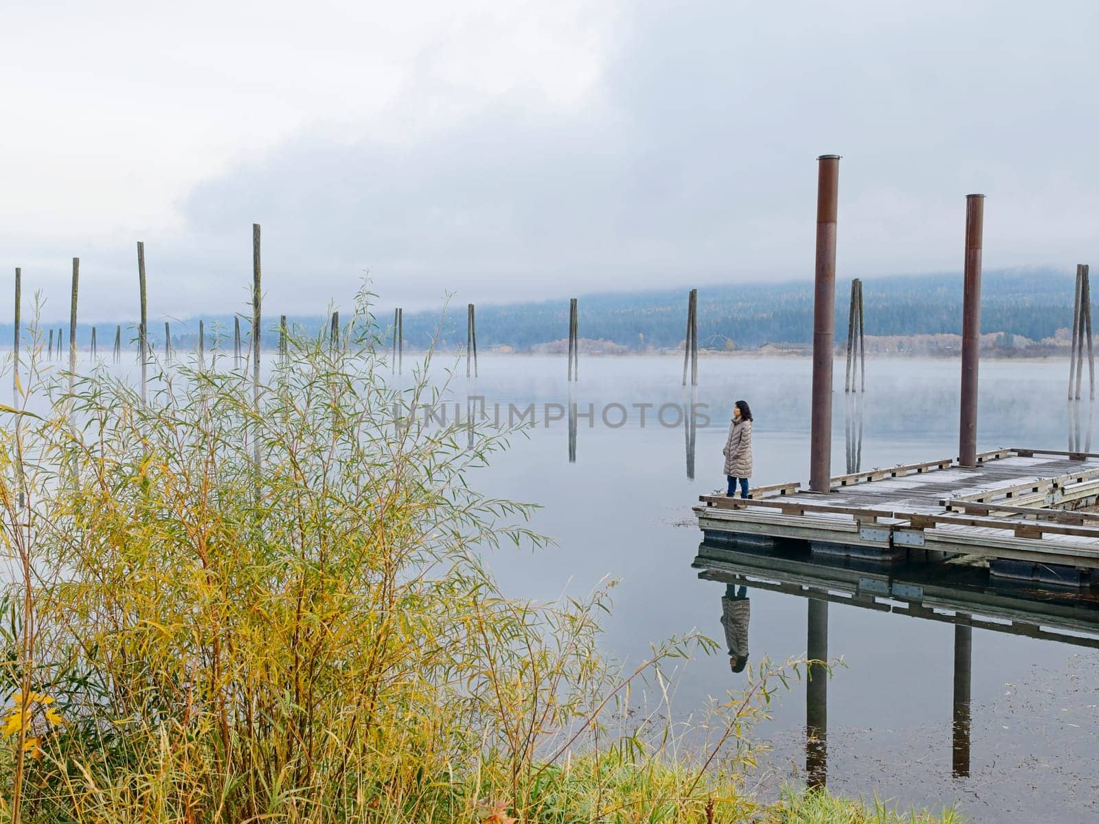 A landscape photo of a woman standing on a dock looking out at the calm water of the Pend Oreille River in eastern Washington.