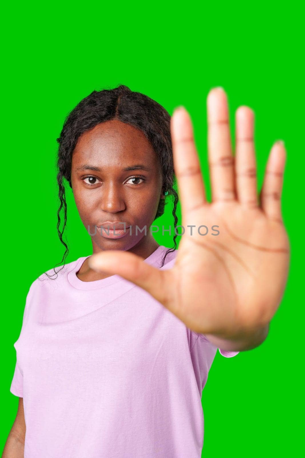 A young woman in a lilac shirt holds her hand up against a bright green background close up
