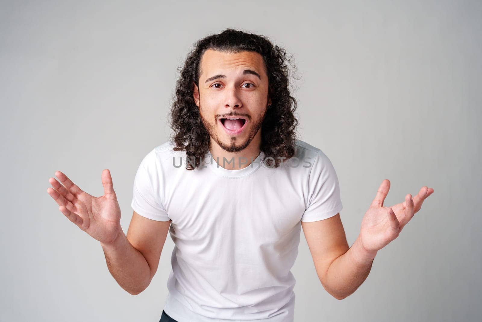 Young man with curly hair expresses surprise in a light-colored setting close up