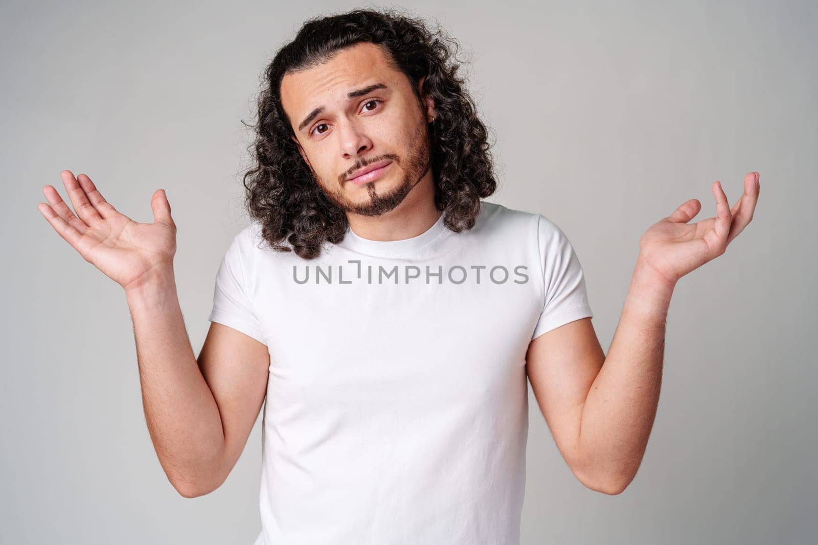 A man with curly hair expressing uncertainty while standing against a neutral background during the day