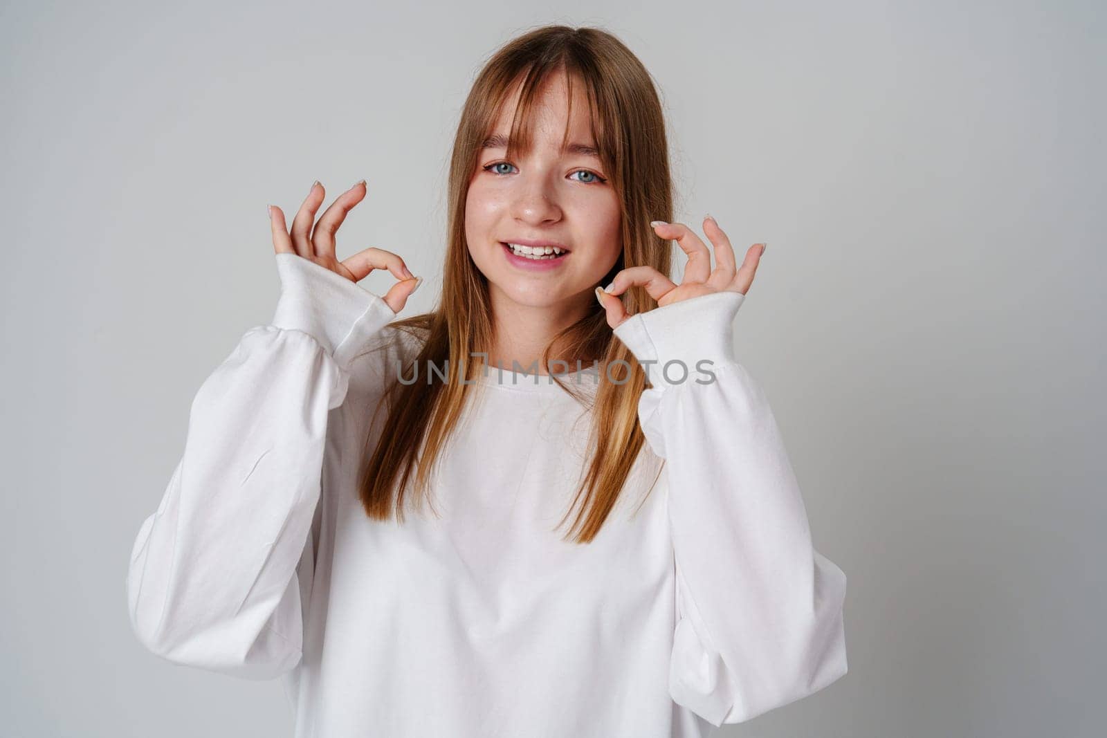 Young woman smiling and making an okay gesture in a bright, minimalistic indoor setting