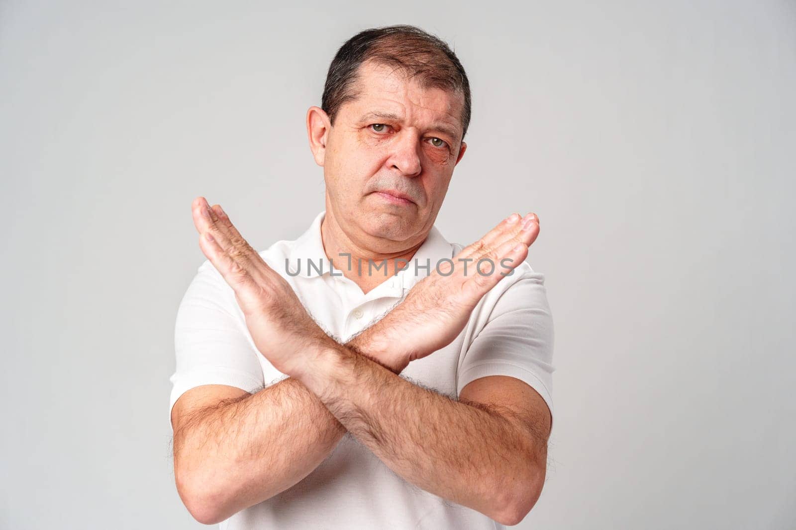 A man making a gesture of refusal with arms crossed against a light background in studio