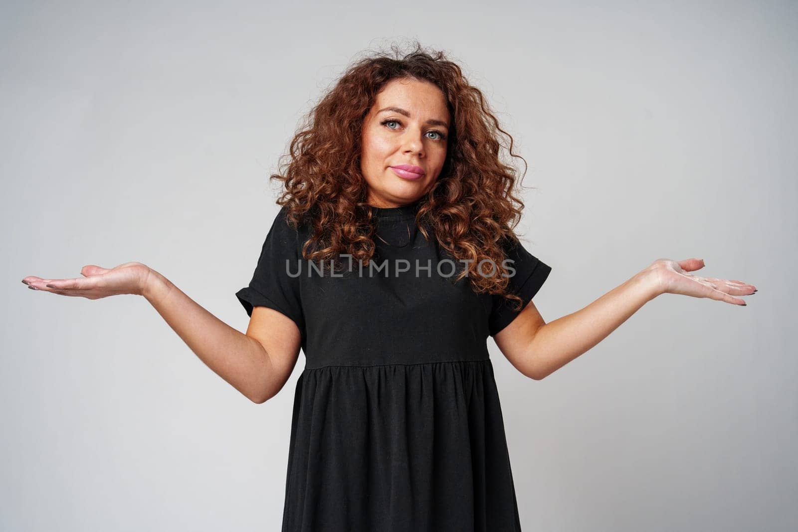 A young woman stands confidently in a black dress, showcasing a playful pose against a plain background close up