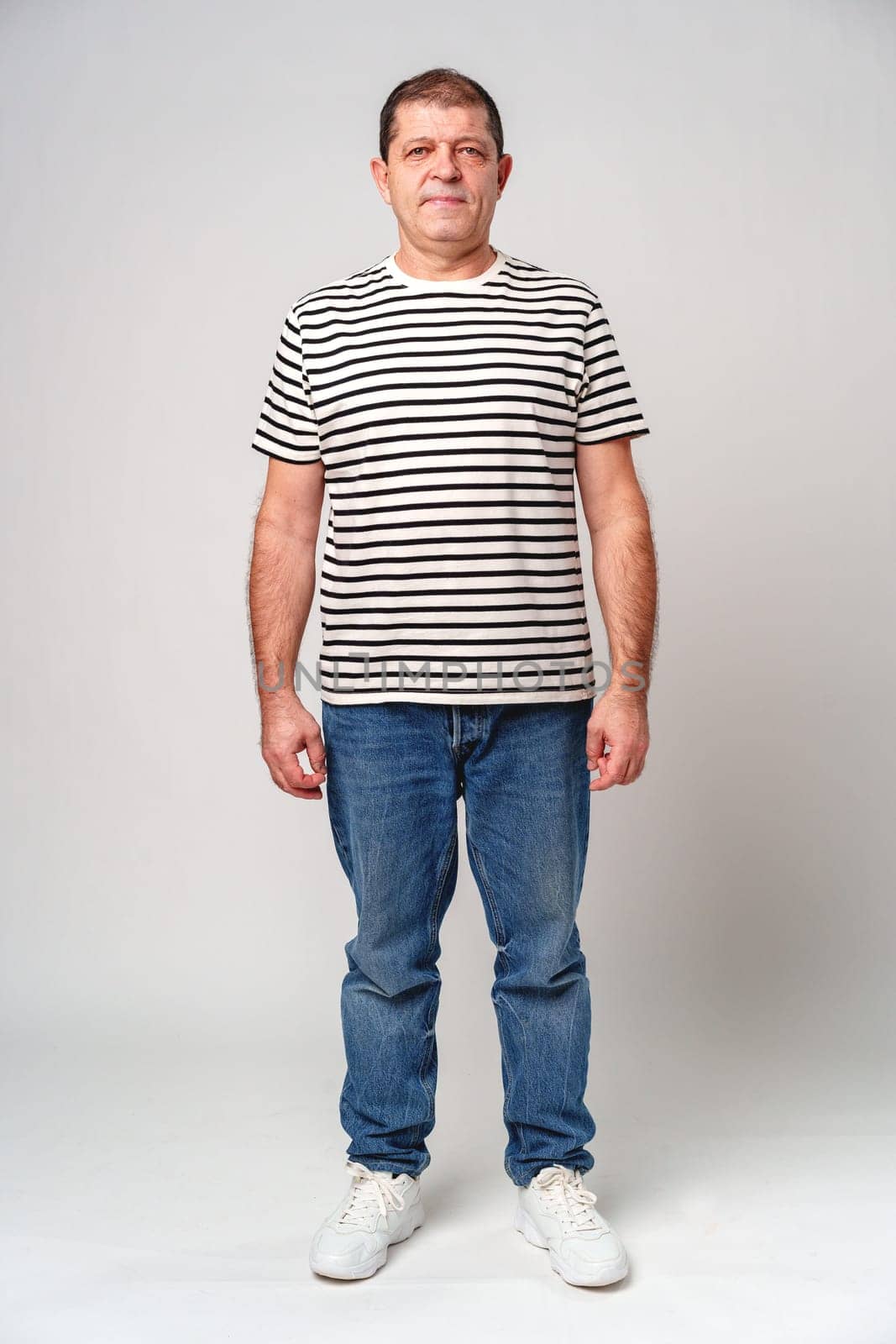 A man stands confidently in a striped shirt, casual jeans with a neutral background in studio